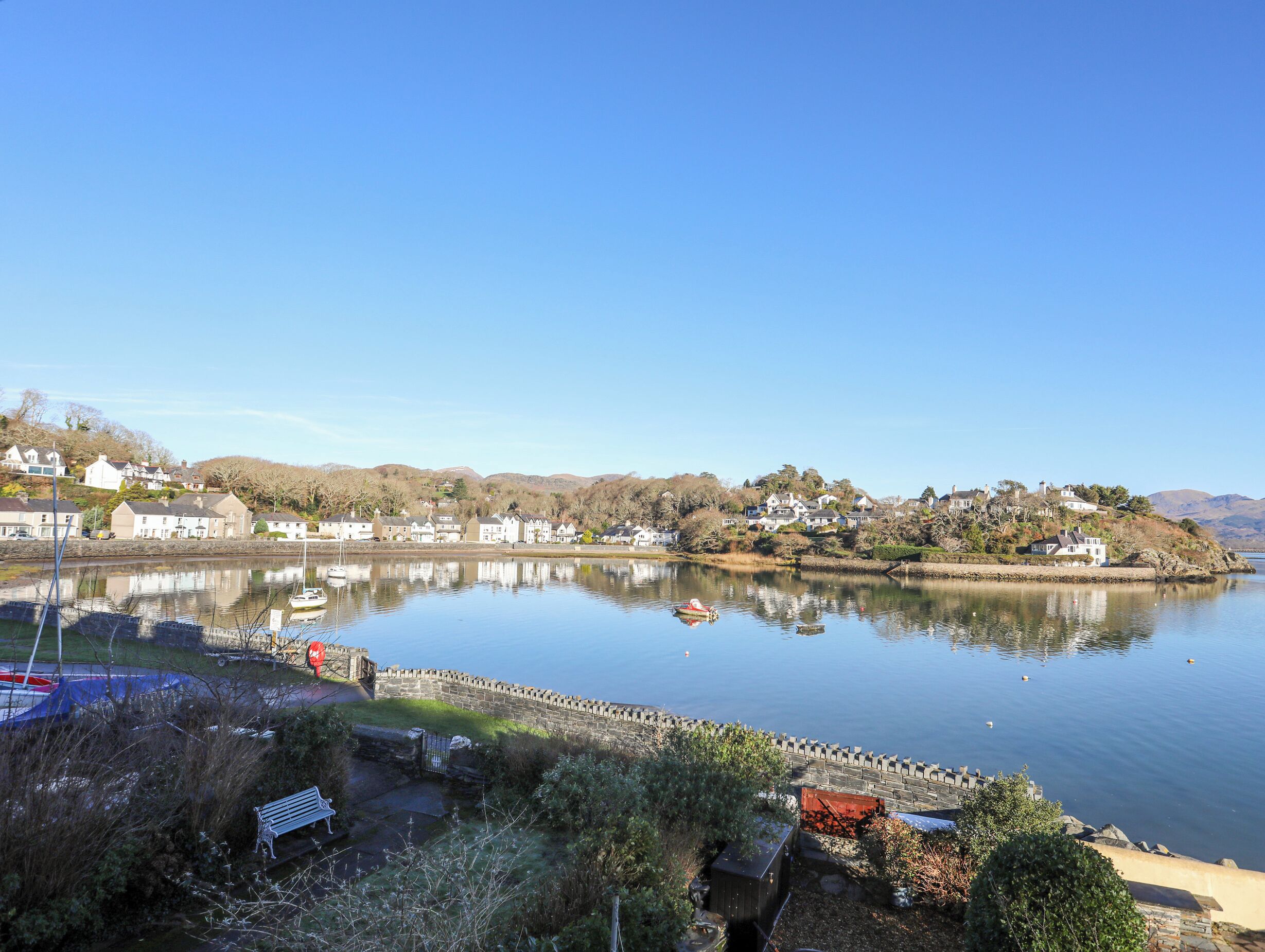Vista de un lago con casas, un muelle y un muro de piedra.