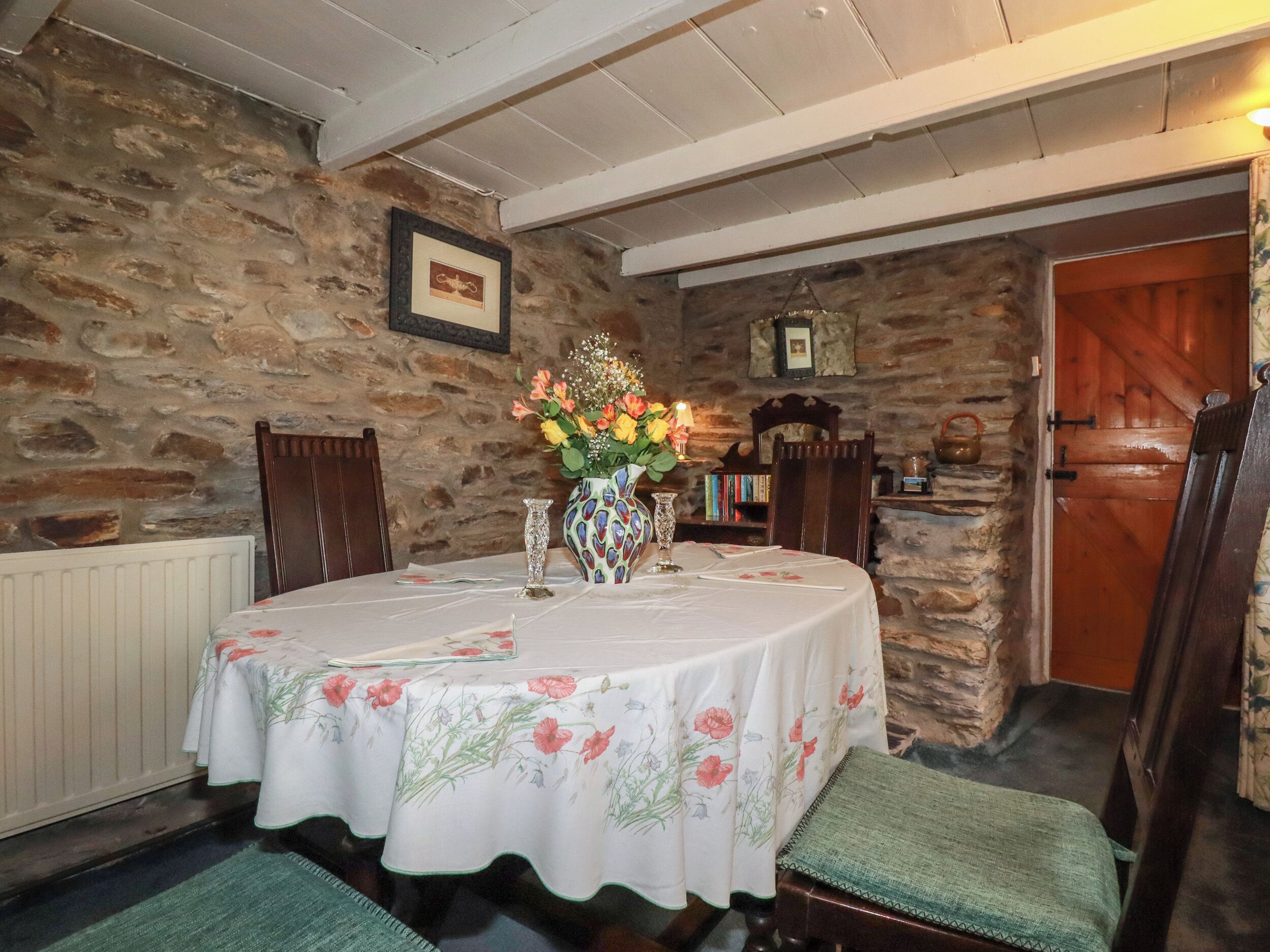 A dining area with a stone wall, a wooden door, and a table set with a floral tablecloth.
