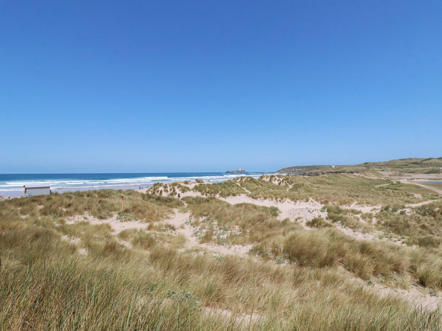 Un paisaje costero con dunas, una playa y un faro a lo lejos.