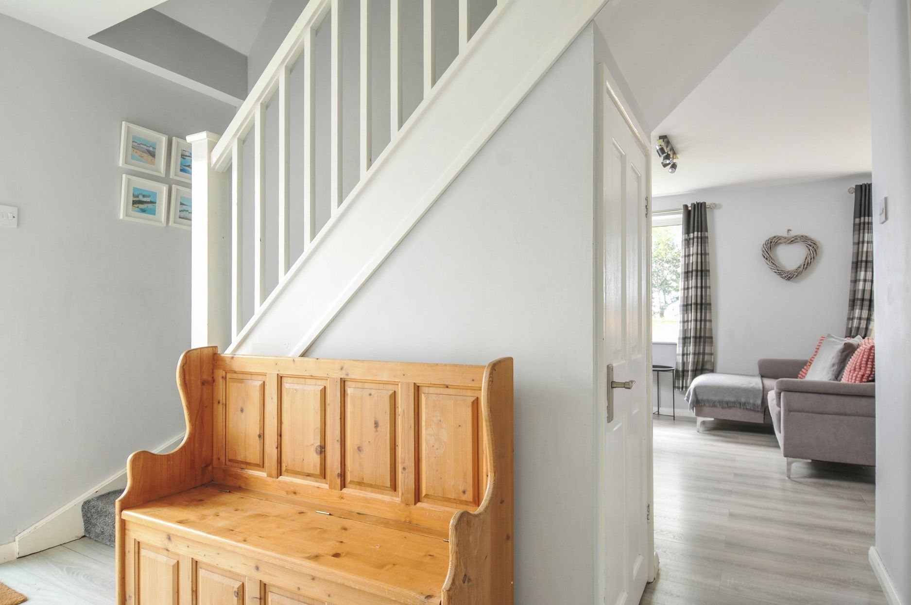A wooden bench in a hallway leading to a living room with a sofa and a heart-shaped decoration on the wall.