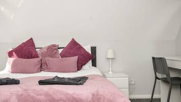 Un dormitorio con una cama, almohadas, una toalla doblada, una mesita de noche con una lámpara y una silla.