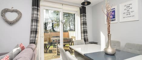 A modern living room with a sofa, dining table, chairs, and a view through a glass door to an outdoor area.