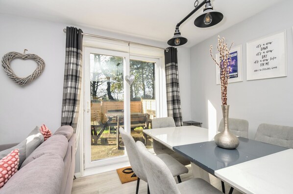 A modern living room with a sofa, dining table, chairs, and a view through a glass door to an outdoor area. - Lewis Lodge (Gunnislake)