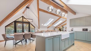 A modern kitchen with a large island, wooden beams, and skylights. - Kolbeh (Ulverston)