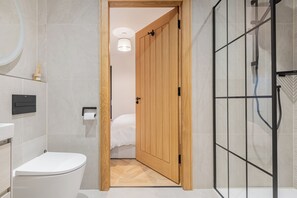 Ein modernes Badezimmer mit Holztür zu Duschbereich, Toilette und Waschbecken.