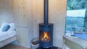 A cozy room with a wood-burning stove, a bed with pillows, and a view of the outdoors. - Broc (Kinvara)
