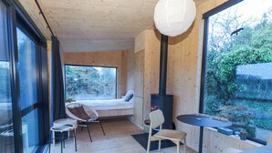 A cozy cabin with a bed, a table, chairs, a fireplace, and large windows offering a view of the outdoors. - Broc (Kinvara)