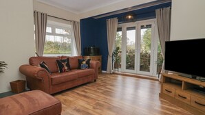 Un salon avec un canapé marron, un téléviseur posé sur un meuble en bois et une porte-fenêtre coulissante donnant sur un jardin.