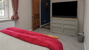 Une chambre à coucher avec un lit, un téléviseur posé sur une commode, une fenêtre avec des rideaux et une porte donnant sur une autre pièce.