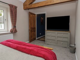 A bedroom with a bed, a television on a dresser, a window with curtains, and a door leading to another room.