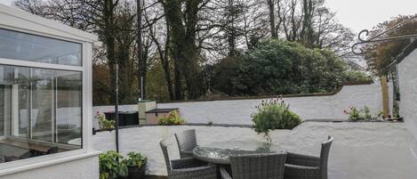 Eine Terrasse mit Korbmöbeln, Topfpflanzen und einer weißen Wand.