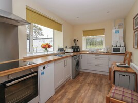 A modern kitchen with a dishwasher, oven, and microwave. There is a wooden countertop and a small dining area with a chair.