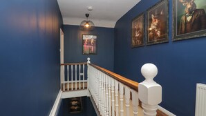 Un escalier avec des balustrades blanches et une main courante en bois, menant à un palier orné d’un tableau encadré et d’un luminaire suspendu.