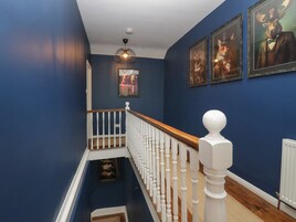 A staircase with white balusters and a wooden handrail, leading to a landing with a framed picture and a hanging light fixture.