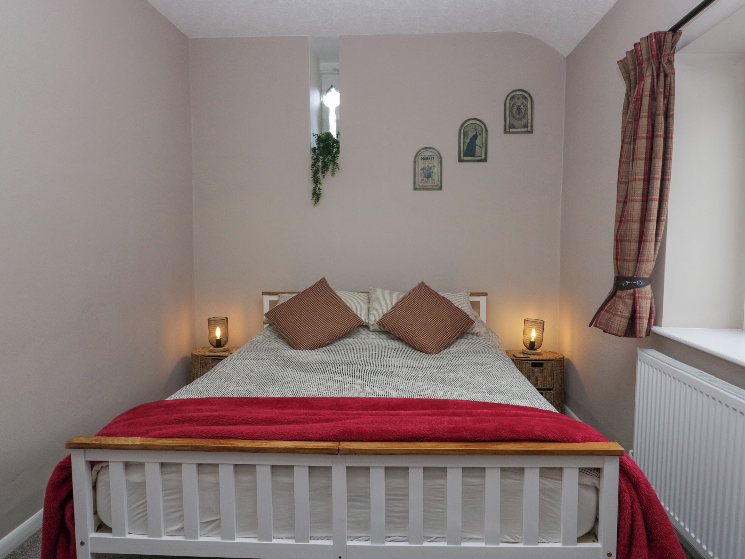 A bedroom with a white bed, two bedside lamps, a red blanket, and a window with a plaid curtain.