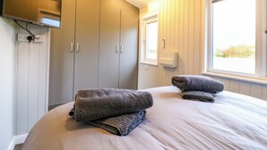 A bedroom with a bed, a TV mounted on the wall, and a window with a view of trees.