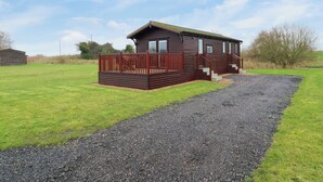 A small wooden cabin with a deck, surrounded by a gravel path and grassy area.