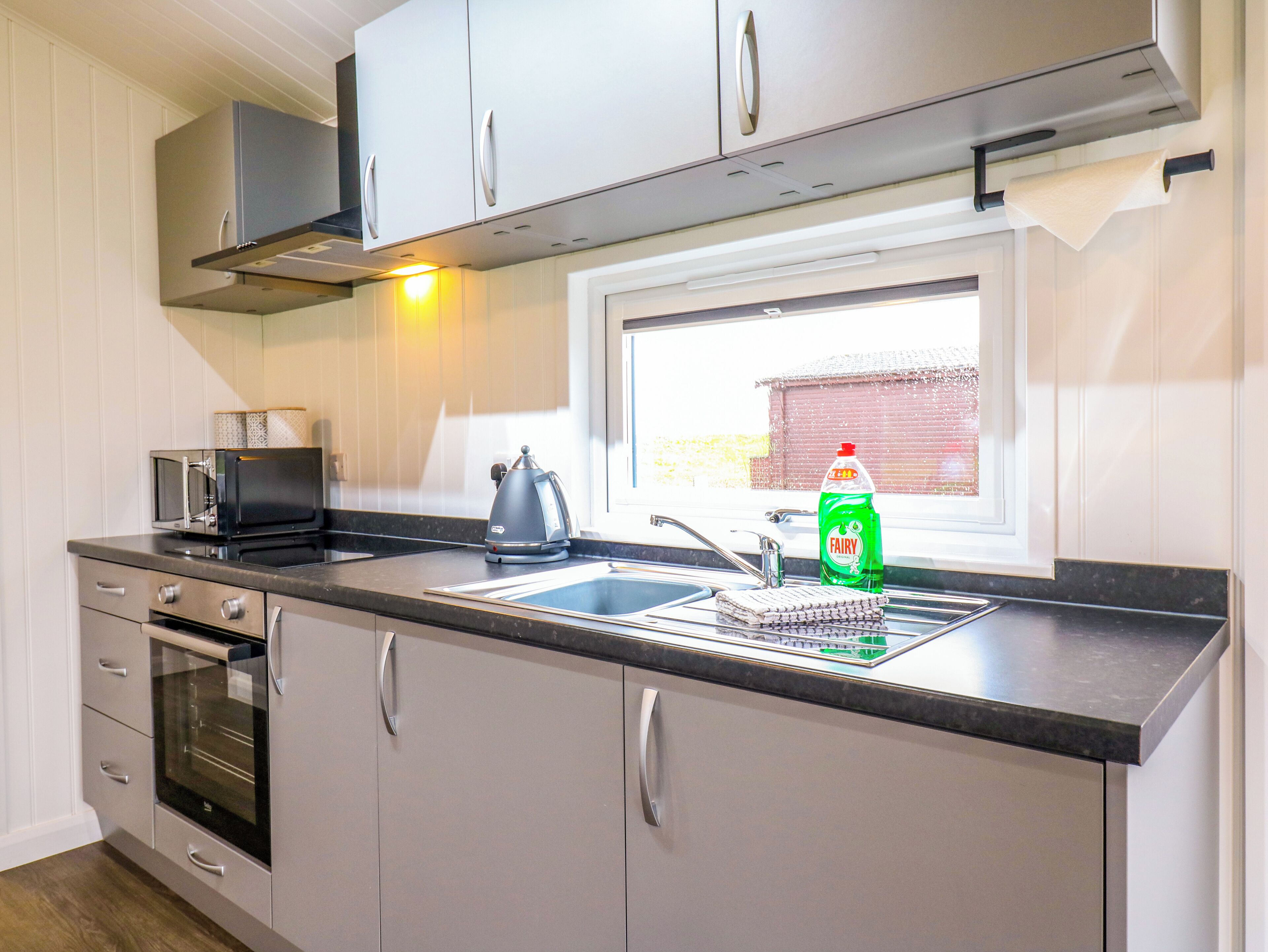 Eine moderne Küche mit eingebautem Backofen, Mikrowelle, Wasserkocher und einem Fenster mit Blick nach draußen.