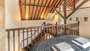 A bedroom with a wooden ceiling, a staircase, and a bed with folded towels. - The Old Smithy (Lynton)
