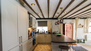 A kitchen with a herringbone floor pattern, wooden beams on the ceiling, and a bar stool near the counter. - The Old Smithy (Lynton)
