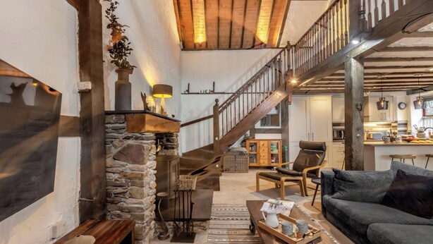 A cozy living room with a stone fireplace, a wooden staircase, and a comfortable seating area. - The Old Smithy (Lynton)