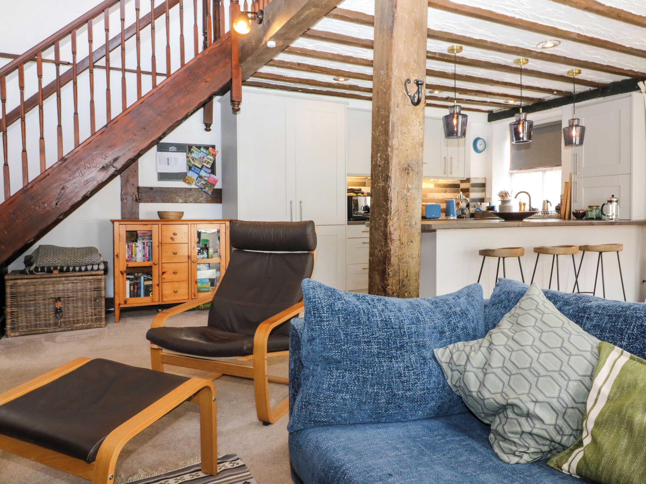 Una sala de estar acogedora con una escalera de madera, un sofá azul, un sillón de cuero y un aparador de madera.