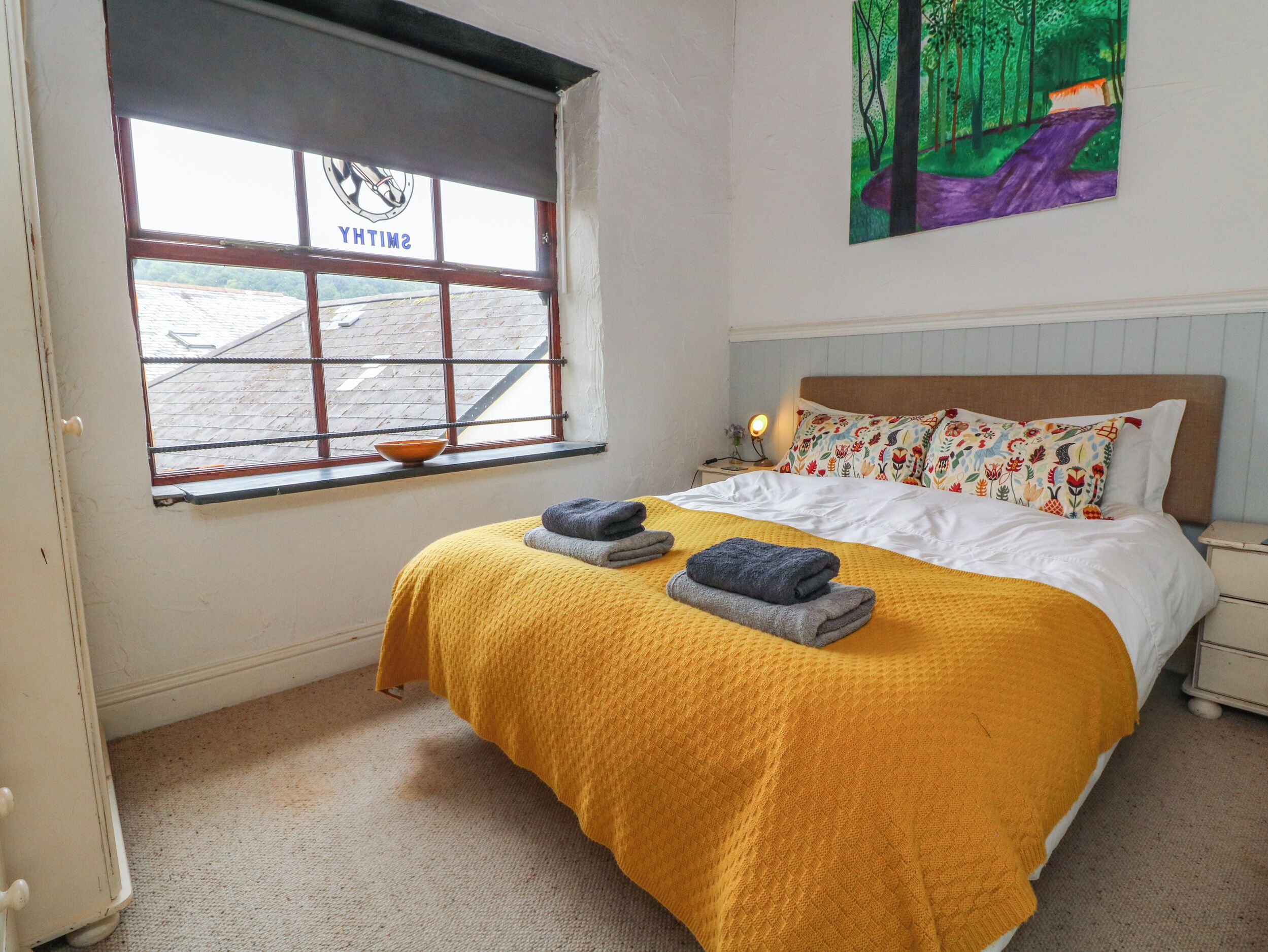 Une chambre à coucher avec un lit, une fenêtre donnant sur un beau paysage, une table de chevet et un tableau accroché au mur.