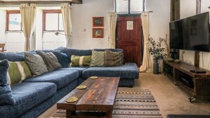 A living room with a blue sofa, wooden coffee table, and a television. - The Old Smithy (Lynton)