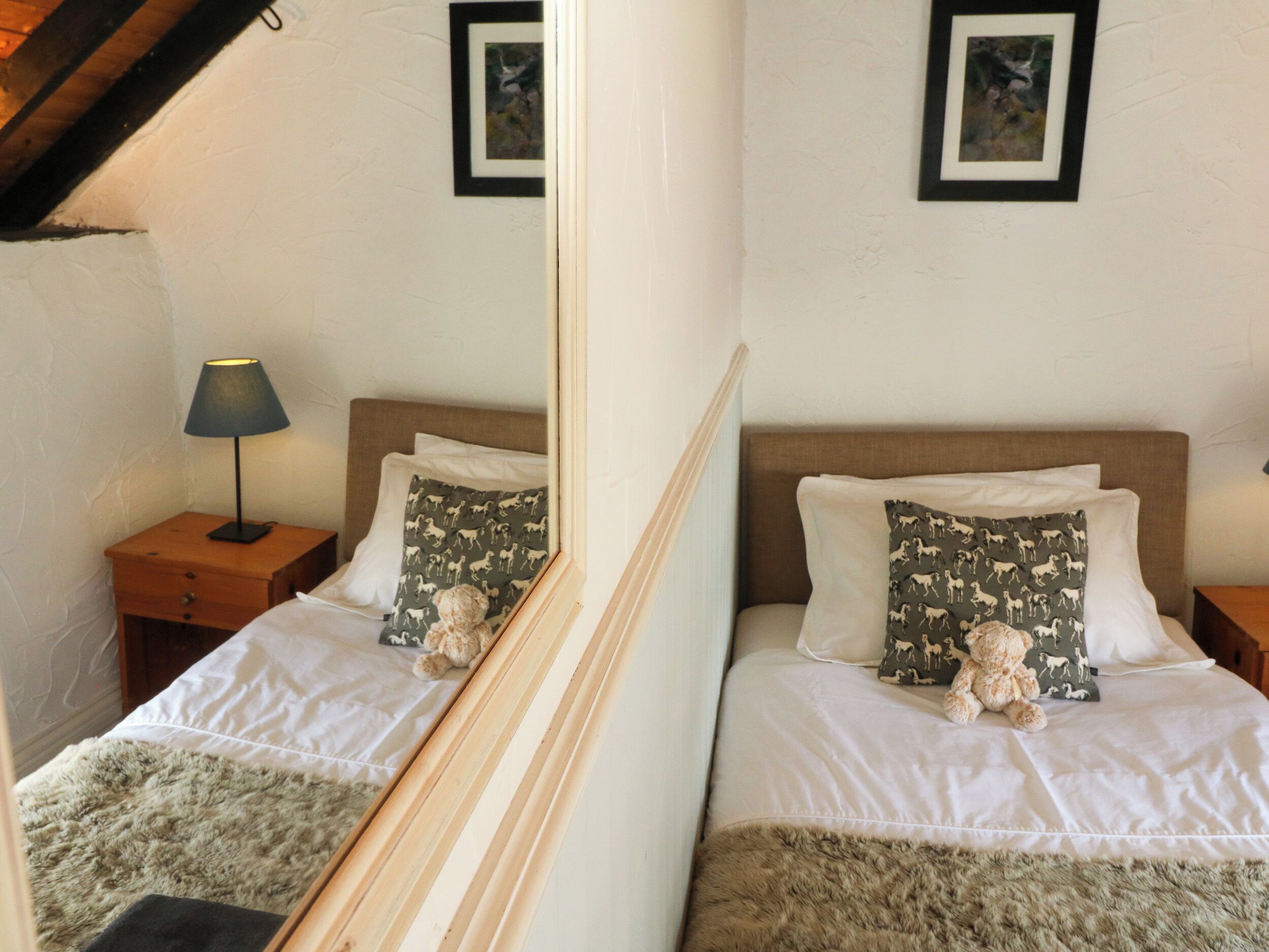 Un dormitorio con dos camas, cada una con almohadas estampadas, una mesita de noche con lámpara y cuadros enmarcados en la pared.