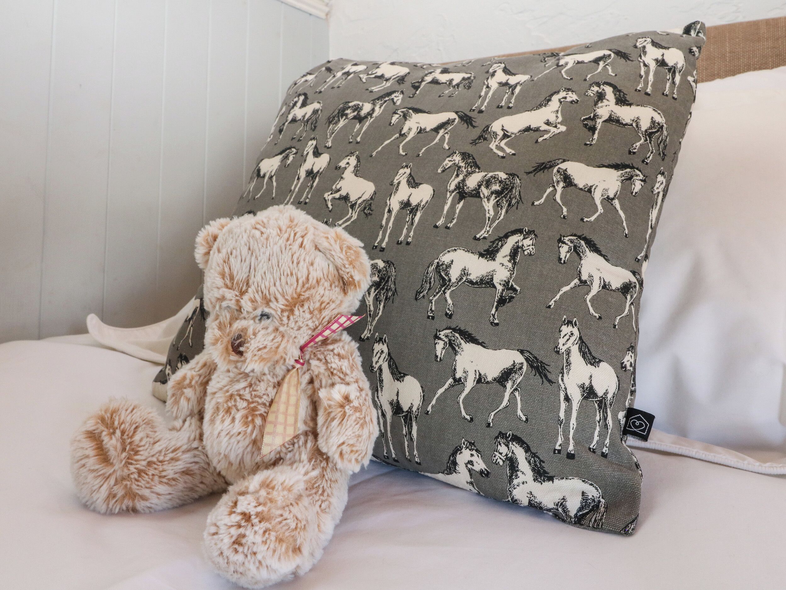 Ein Teddybär sitzt neben einem Kissen mit Pferde-Motiv.