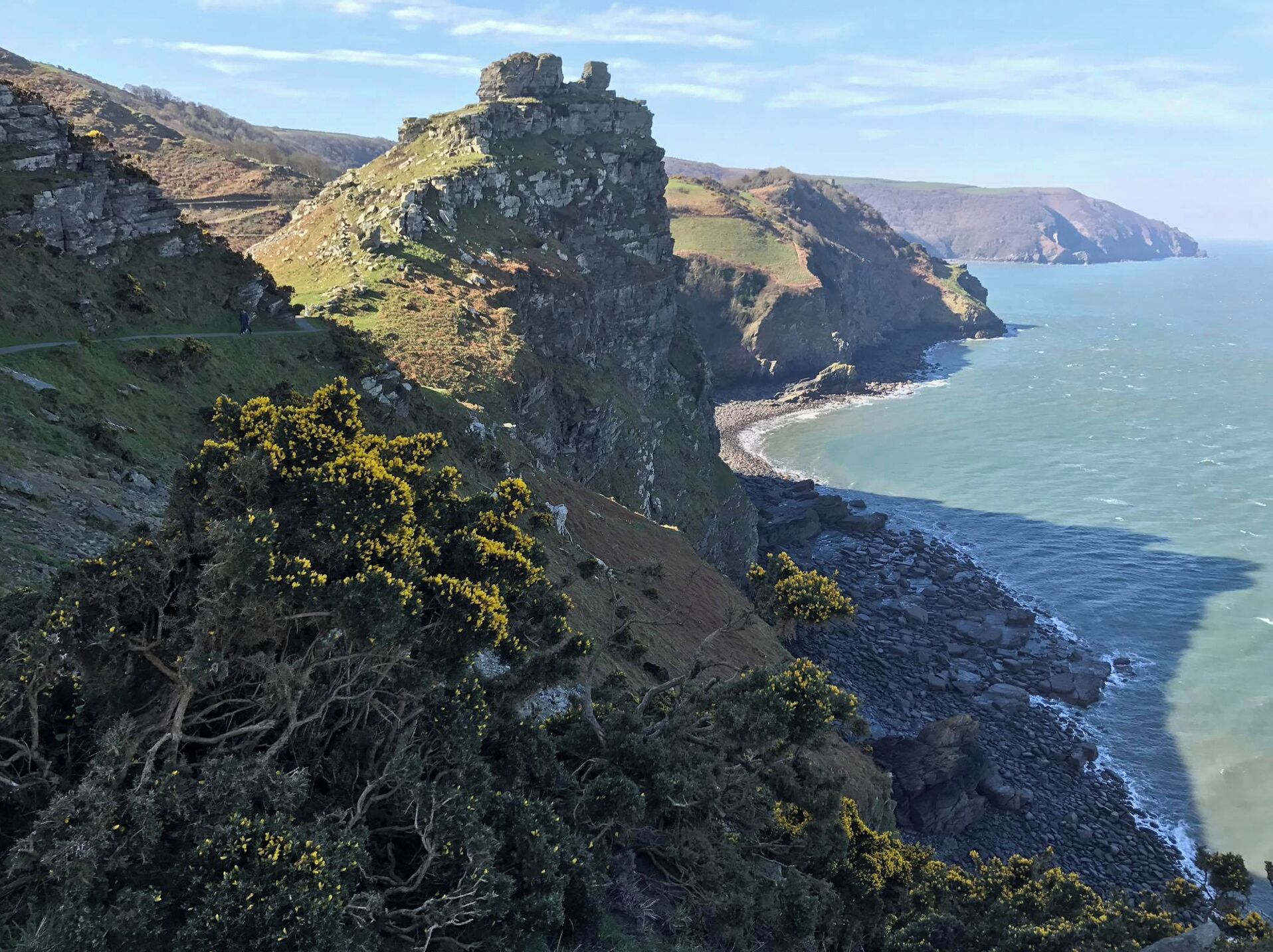 A coastal landscape with rocky cliffs, a path, and a view of the sea.