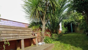 A wooden deck with a brick wall and a palm tree in the background. - 20 Keay Heights (St Austell)