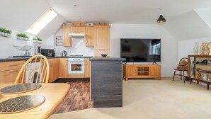 A compact kitchen with wooden cabinets, a built-in oven, and a large TV. - 20 Keay Heights (St Austell)