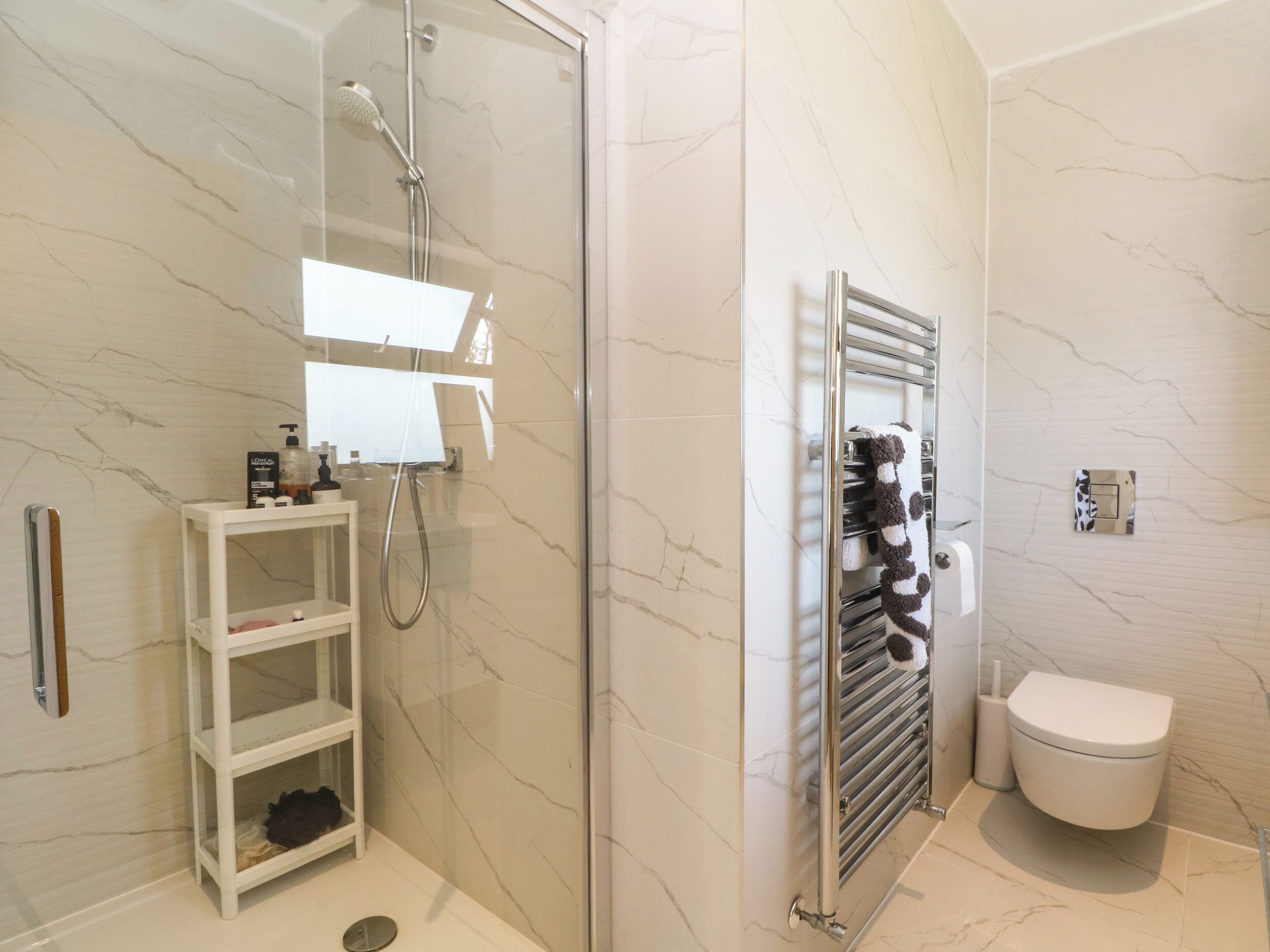 Un baño moderno con ducha de vidrio, inodoro blanco y perchero para toallas.