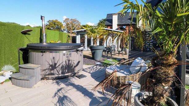 Un jacuzzi, mobiliario exterior y una planta en maceta en un patio trasero.