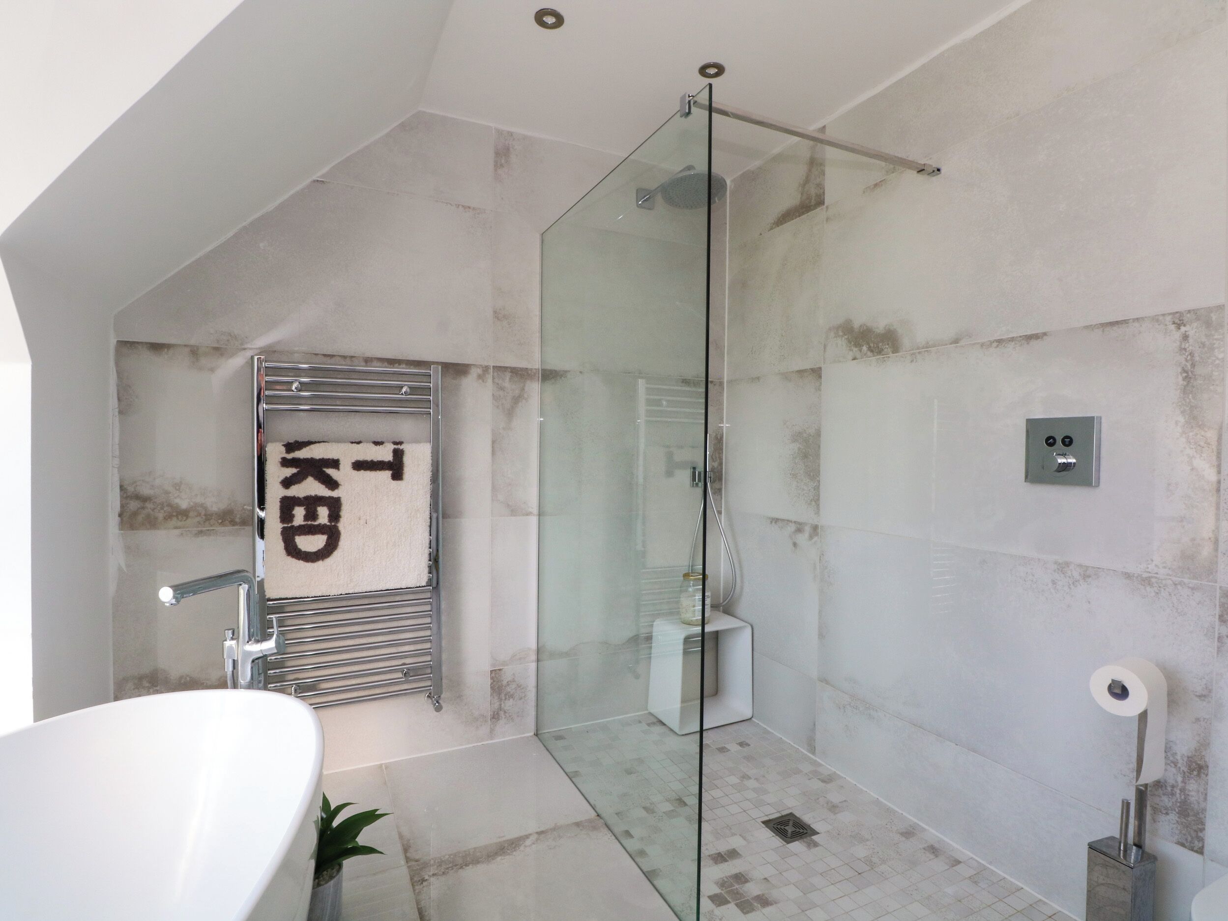 A modern bathroom with a glass-enclosed shower, a white bathtub, and a towel rack with a towel hanging.
