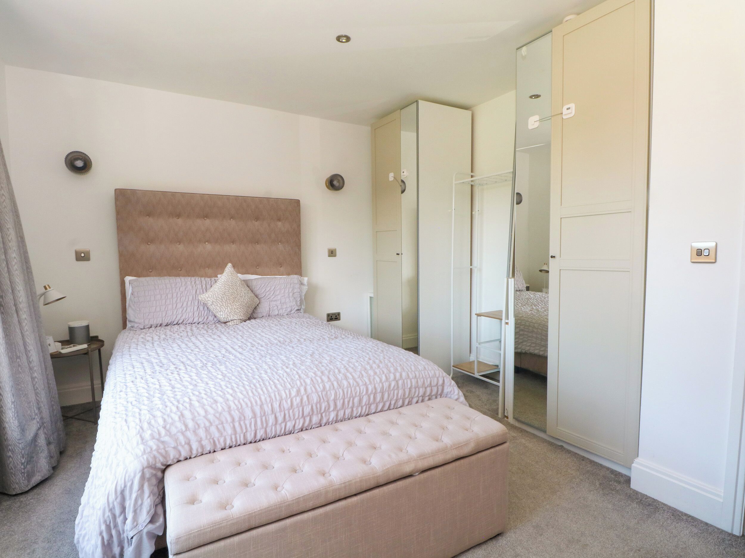 A bedroom with a large bed, a bedside table, a mirror, and a wardrobe.