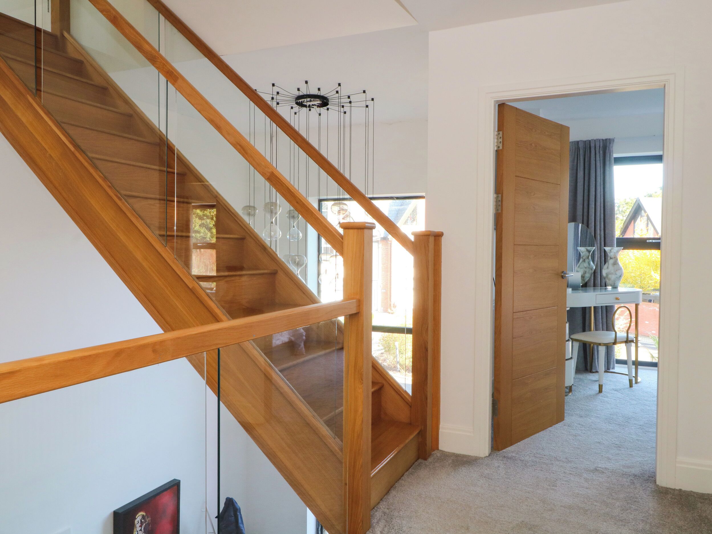 A wooden staircase with glass railings leading to a room with a desk and chair, a door to another room, and a view of the outside.