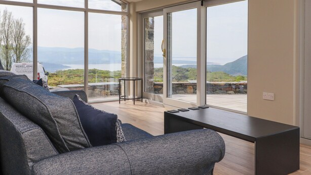 A modern living room with large windows, a sofa, a coffee table, and a hanging light fixture. - Beudy Mawr (Garndolbenmaen)