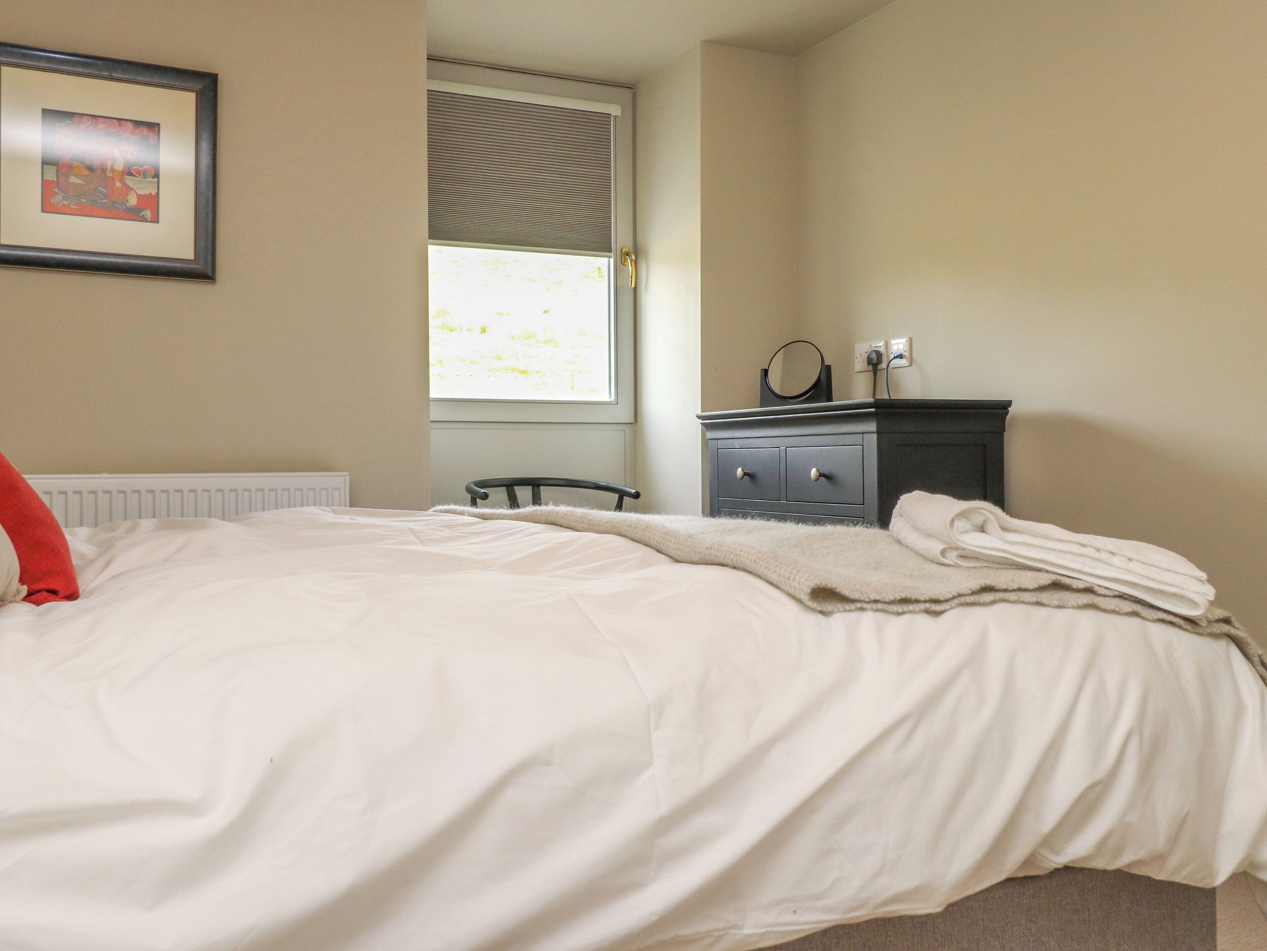 A bedroom with a bed, a dresser, a radiator, a window with blinds, and a framed picture on the wall.