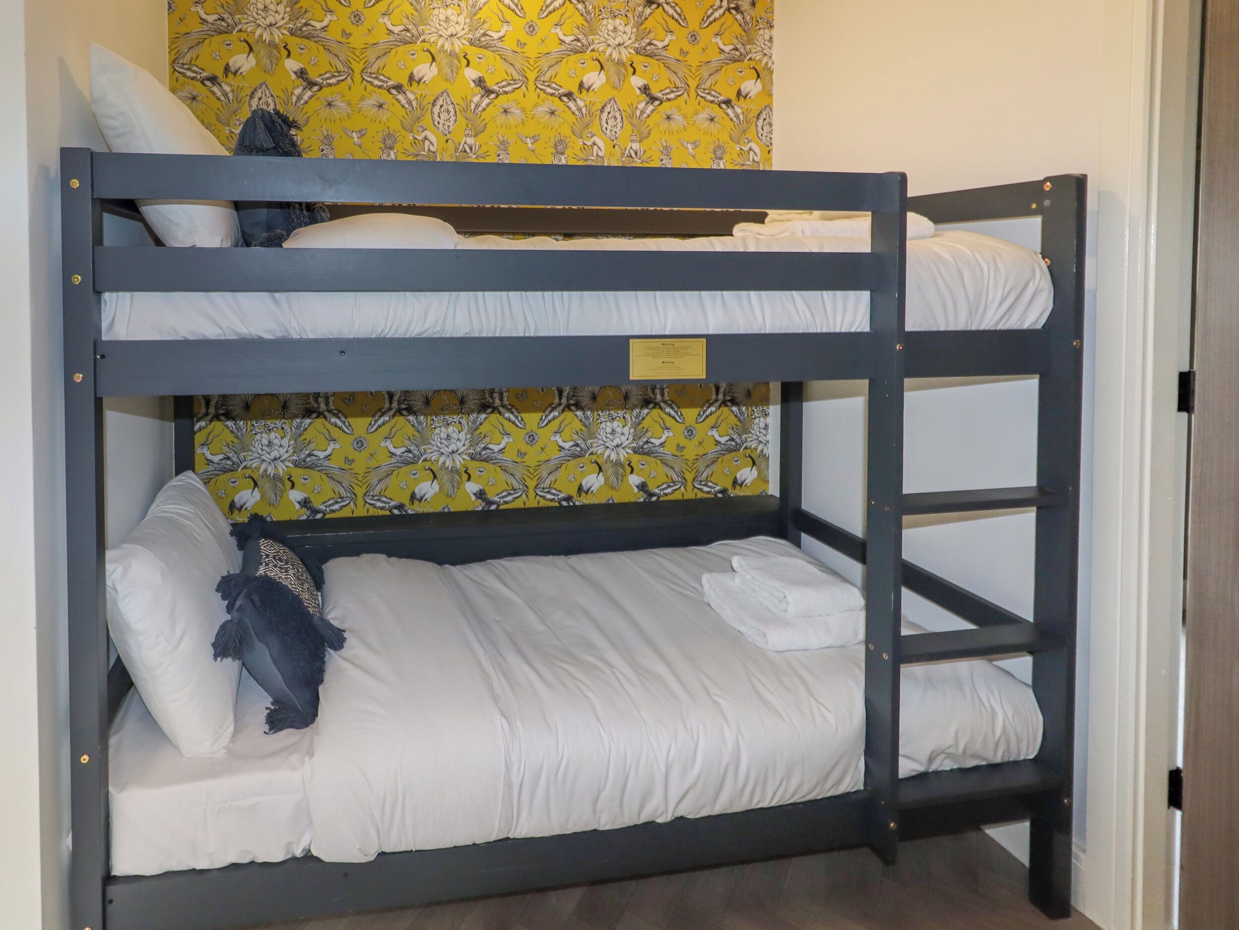 A bunk bed with white bedding and a yellow floral wallpaper.