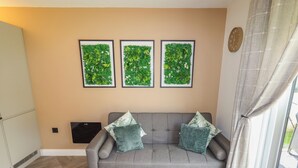 Ein Wohnzimmer mit grauem Sofa, zwei Kissen, einem Fischgrätparkett und drei gerahmten botanischen Wandbildern.