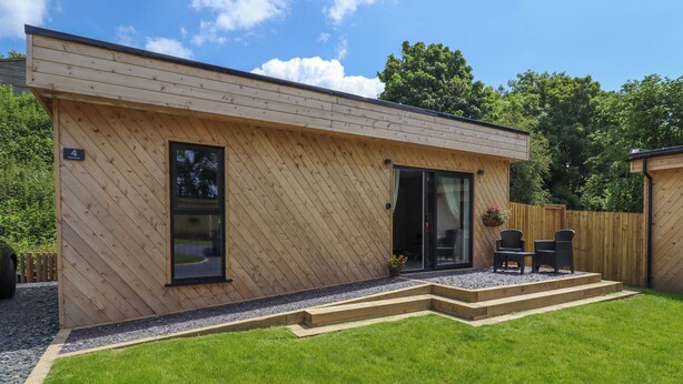 Ein modernes Holzhaus mit Terrasse, einer Glasschiebetür und einer kleinen Sitzgelegenheit im Freien.