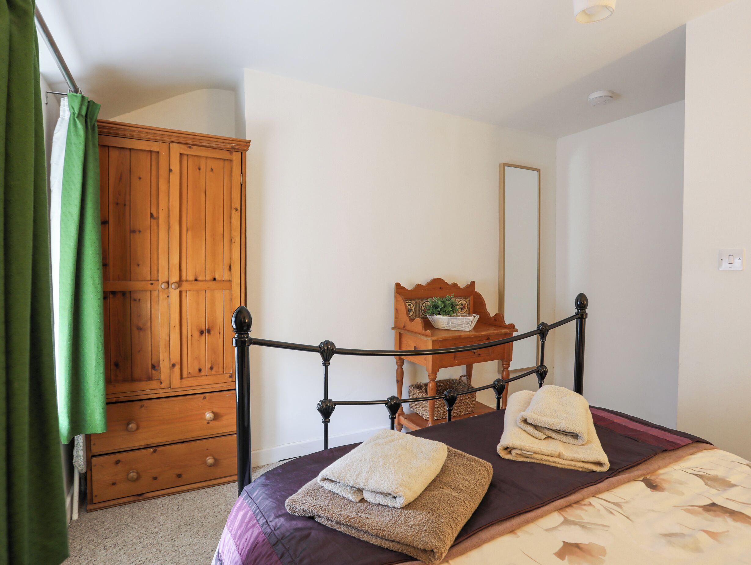 A bedroom with a bed, a wooden wardrobe, a wooden chair, and a mirror on the wall.