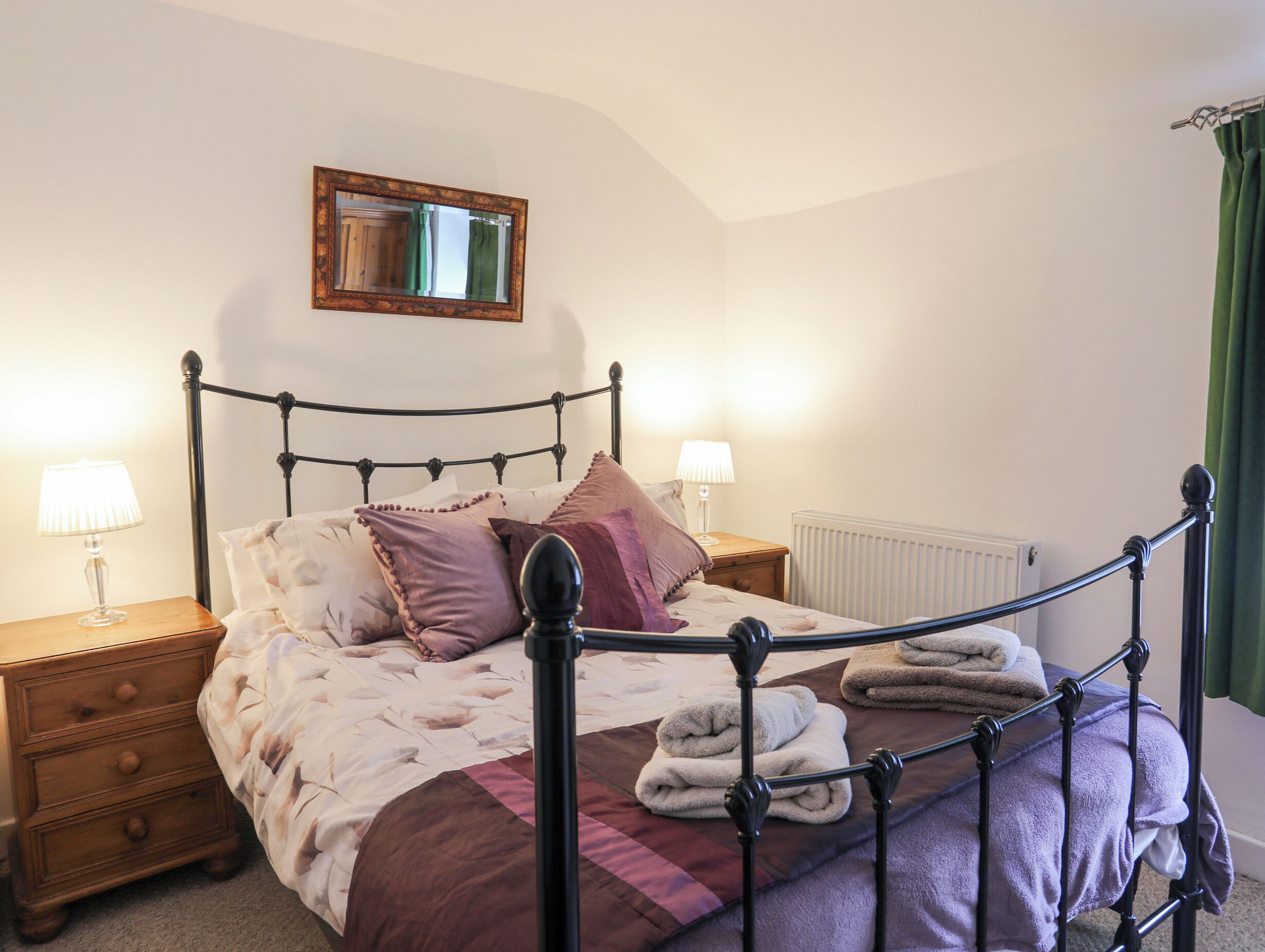 Un lit bien fait, avec un cadre en métal, deux tables de chevet avec des lampes et un radiateur au mur.
