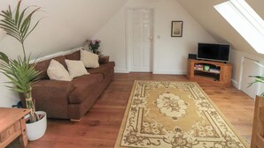 Ein gemütliches Wohnzimmer mit einem braunen Sofa, einem großen Teppich, einem Holz-TV-Schrank und einem Deckenventilator.