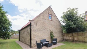 Ein Steinhaus mit rotem Dach, einem kleinen Fenster und einer Terrasse mit Gartenmöbeln.