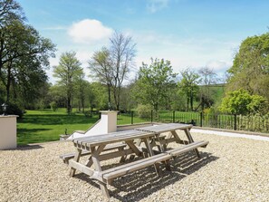 Une table de pique-nique est installée sur une surface de gravier, avec un champ herbeux et des arbres en arrière-plan.