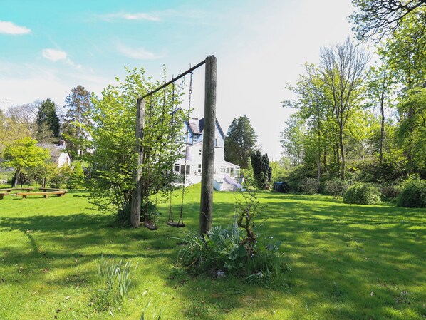 A grassy garden with a wooden swing set and a white building in the background. - Serenity House, The Retreat (Llangammarch Wells)