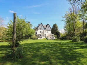 Une grande maison à deux étages, dotée d’une façade en pierre, d’une cheminée imposante et d’une pelouse bien entretenue.
